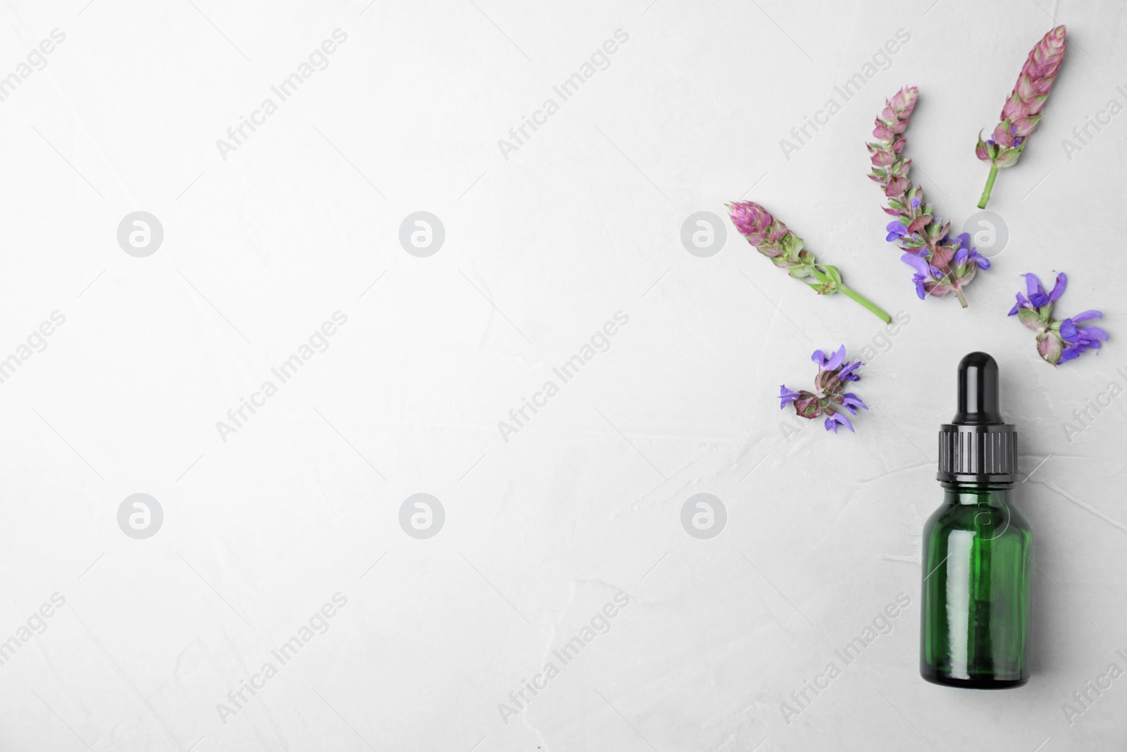 Photo of Bottle of sage essential oil and flowers on light table, flat lay. Space for text