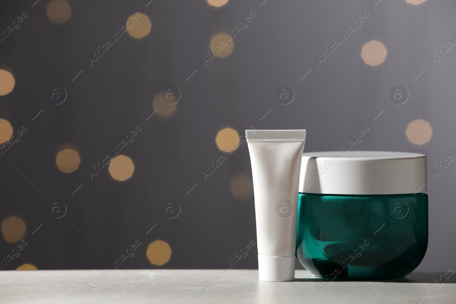 Photo of Skin care products on white table against blurred lights, space for text