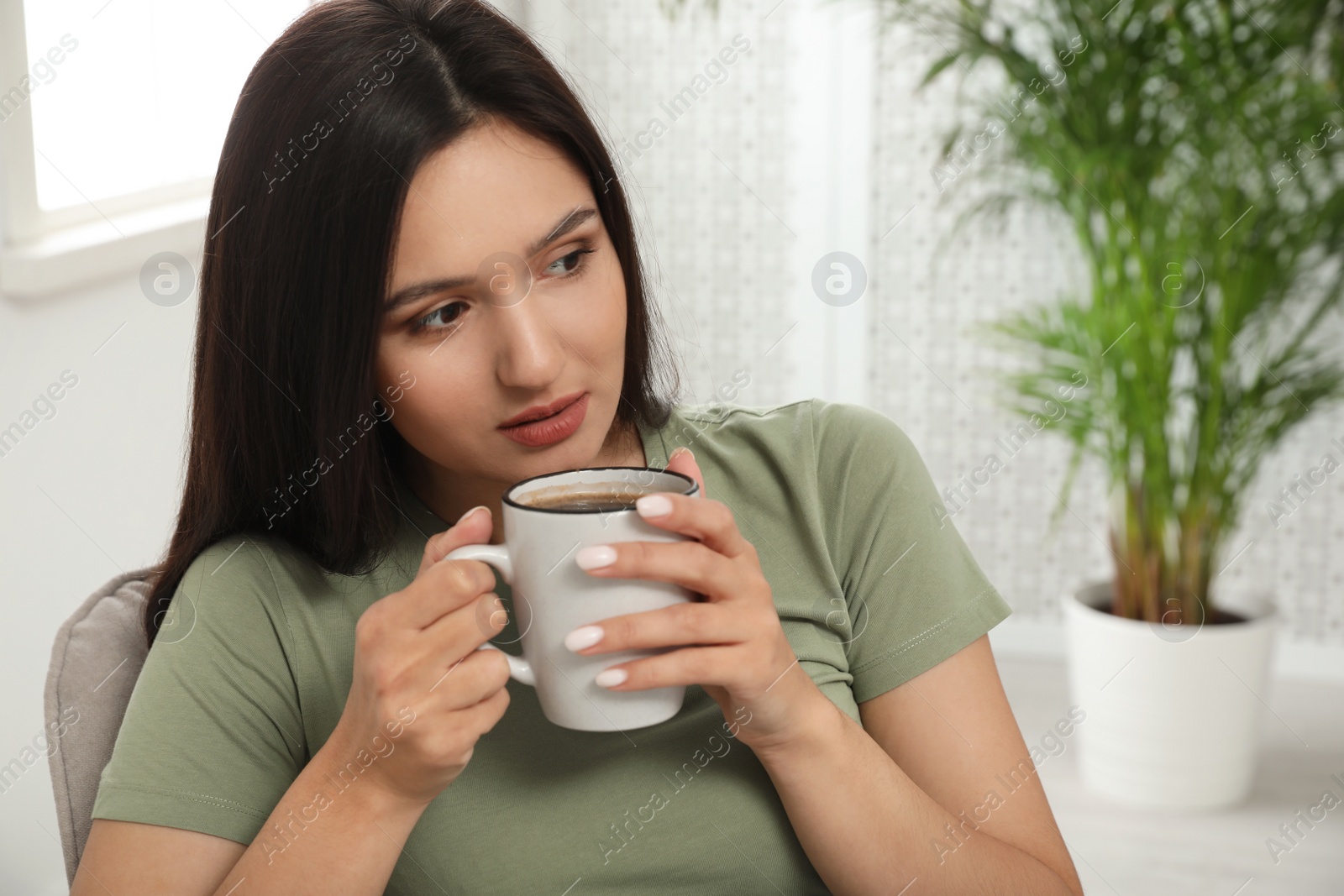 Photo of Young woman with cup of drink relaxing at home