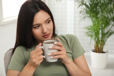 Young woman with cup of drink relaxing at home