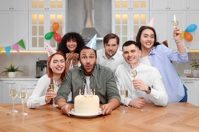 Happy friends with tasty cake celebrating birthday in kitchen