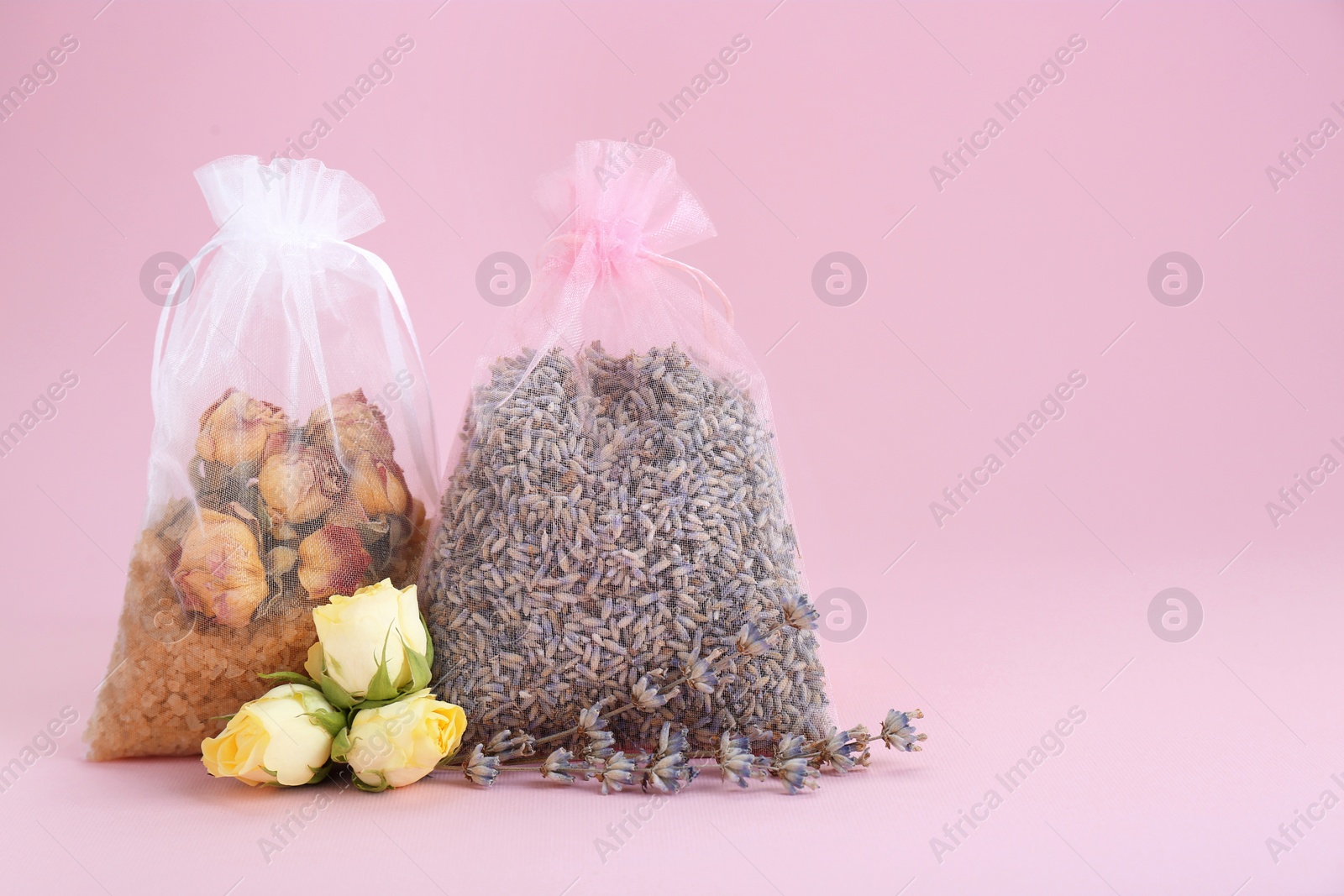 Photo of Scented sachets with dried roses, sea salt and lavender flowers on pink background, space for text