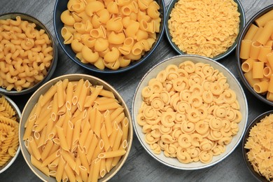 Photo of Different types of pasta on grey table, flat lay