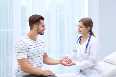 Doctor checking young man's pulse in hospital