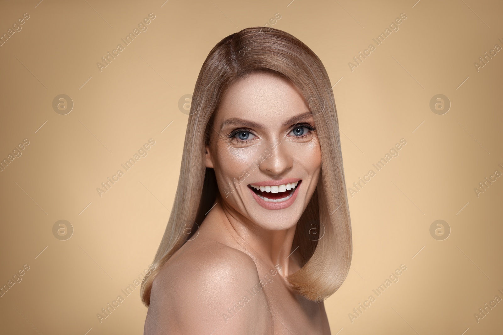 Image of Portrait of attractive woman with blonde hair smiling on dark beige background