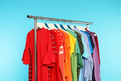 Wardrobe rack with different bright clothes on color background