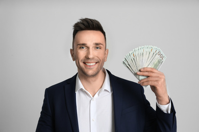 Happy man with cash money on light grey background