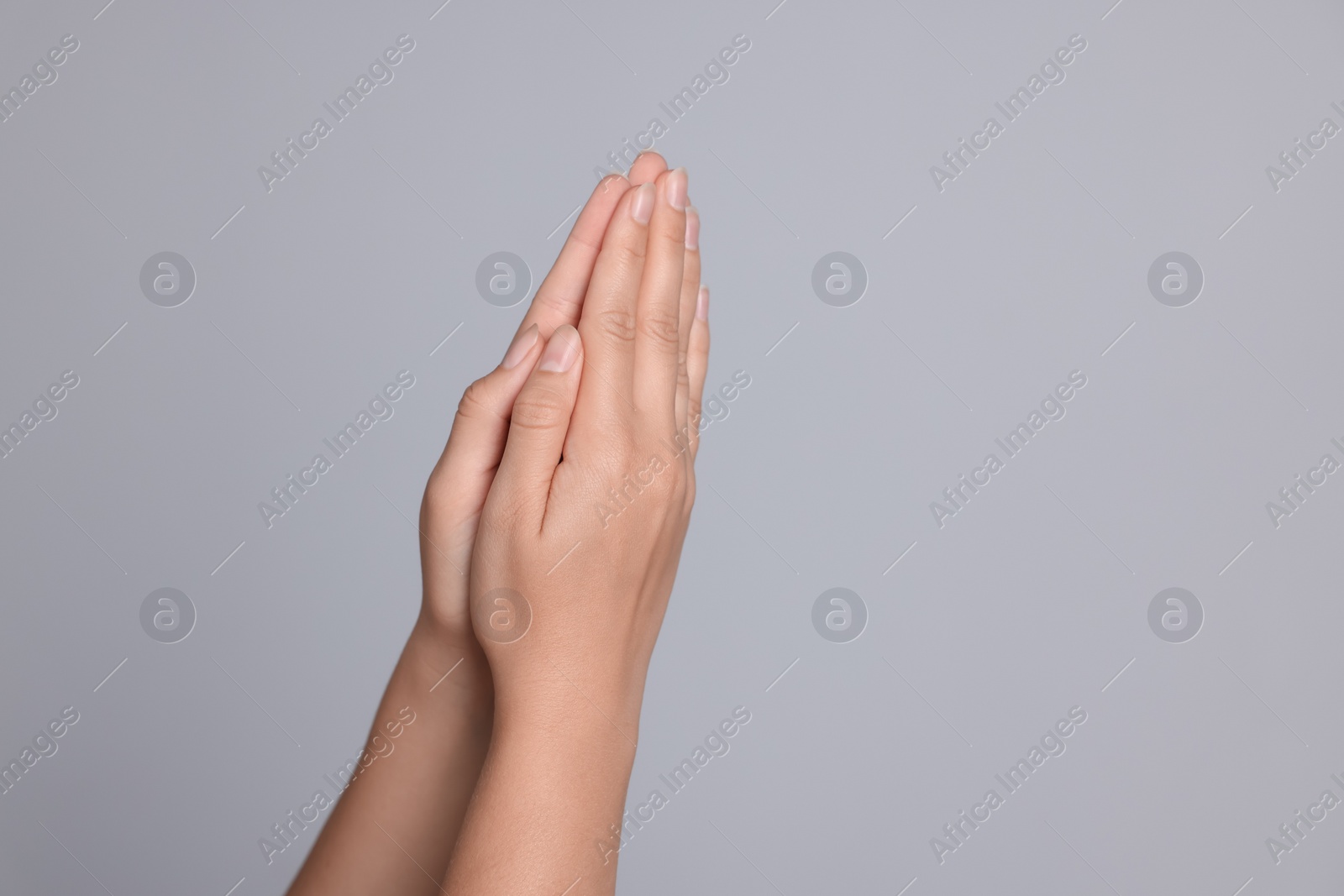 Photo of Woman holding hands clasped while praying against light grey background, closeup. Space for text