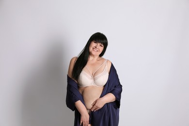 Photo of Beautiful overweight woman in beige underwear and silk robe on light background. Plus-size model