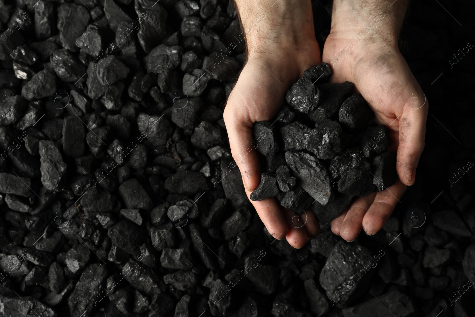 Photo of Man holding coal in hands over pile, top view. Space for text
