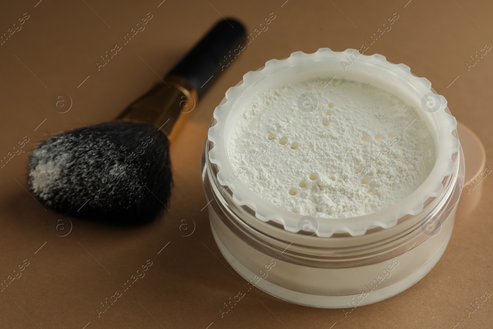 Photo of Rice loose face powder and makeup brush on brown background, closeup