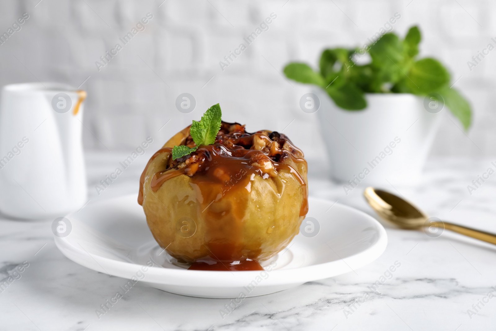 Photo of Delicious baked apple with nuts, caramel and mint served on white marble table