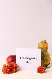 Photo of Thanksgiving day, holiday celebrated every fourth Thursday in November. Card, apple, pumpkin and chrysanthemum flowers on white wooden table, space for text