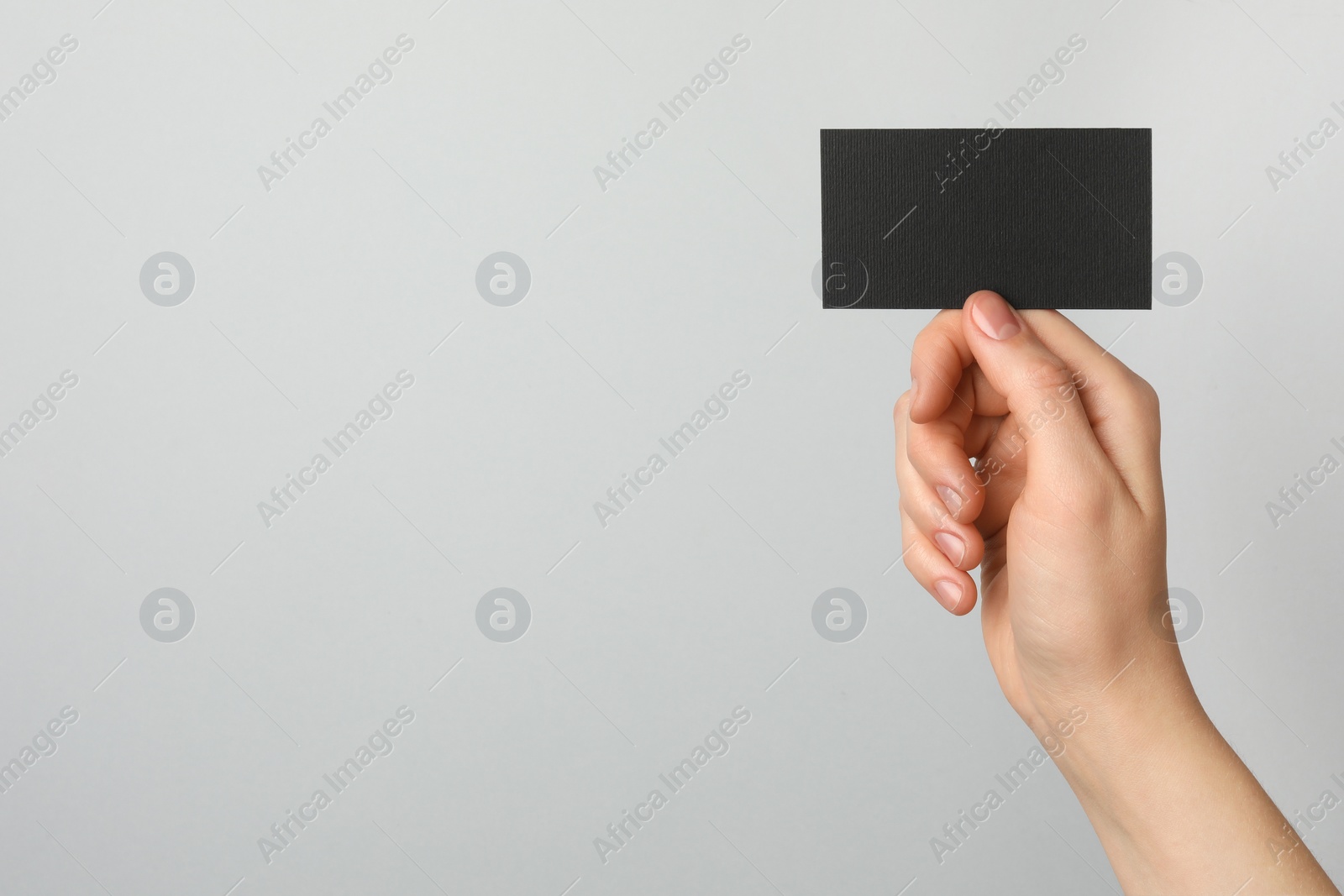 Photo of Woman with blank black business card on light grey background, closeup. Mockup for design