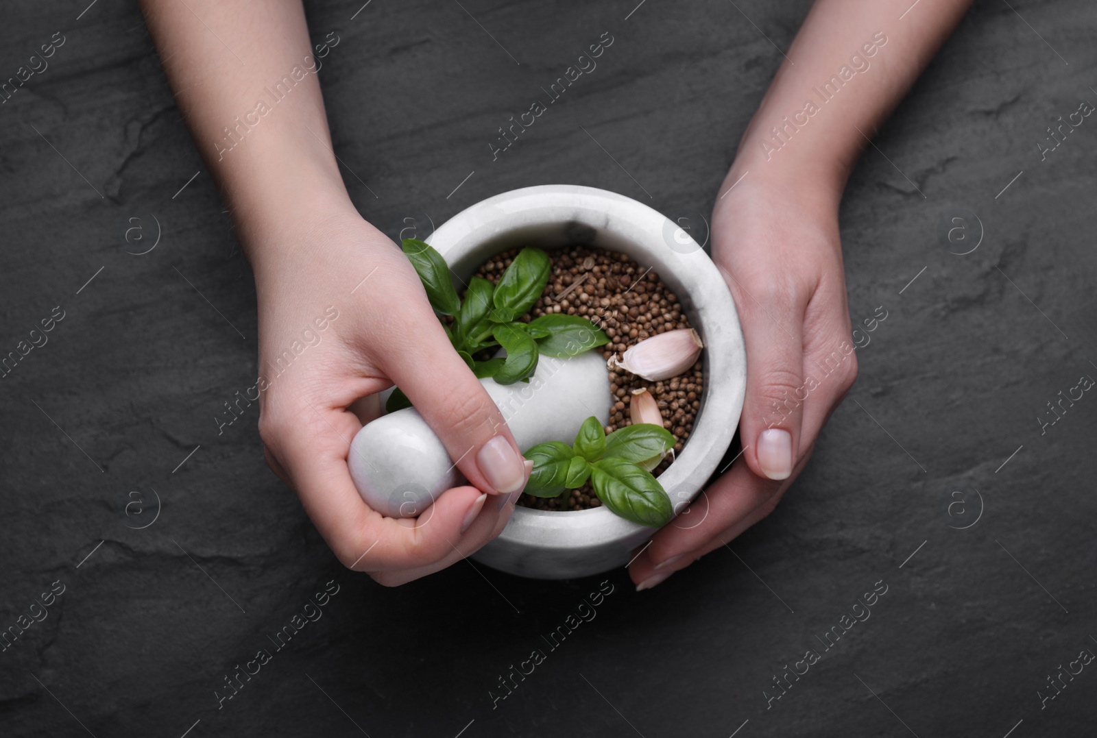 Photo of Woman mixing peppercorns, basil and garlic in mortar at black table, top view