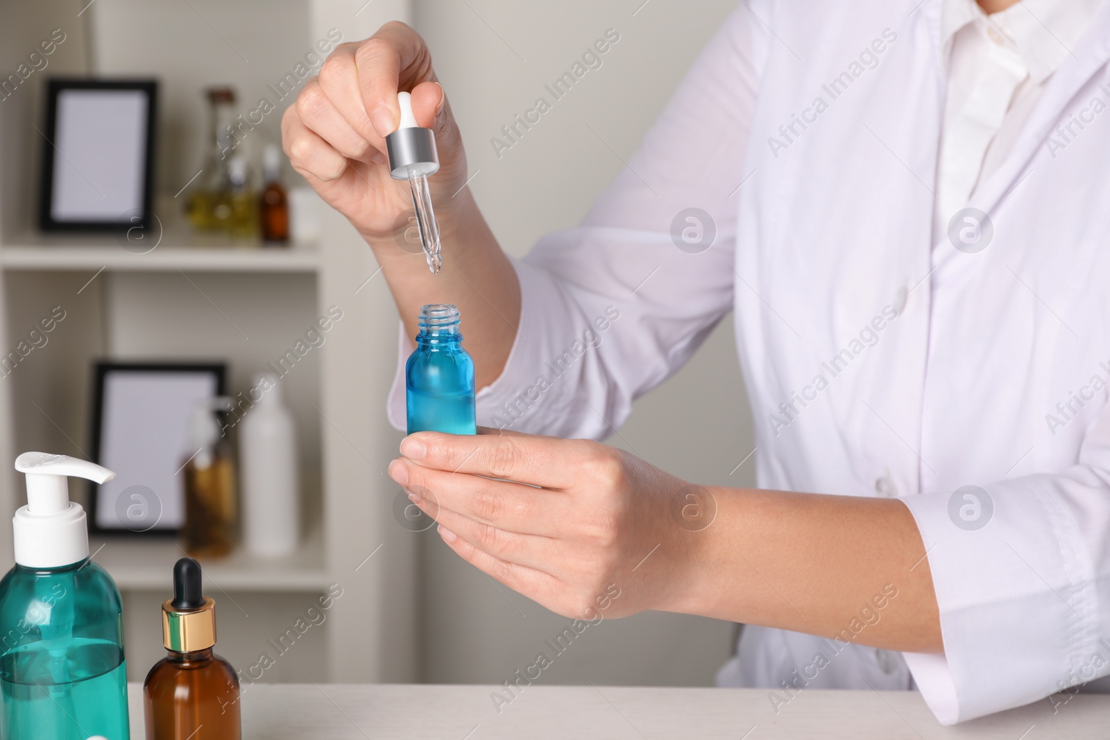 Photo of Dermatologist developing cosmetic product at white table indoors, closeup