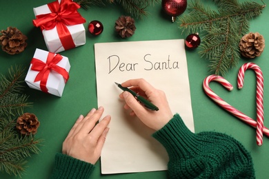 Photo of Top view of woman writing letter to Santa at green table, closeup