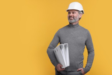 Photo of Architect in hard hat holding folders on orange background. Space for text
