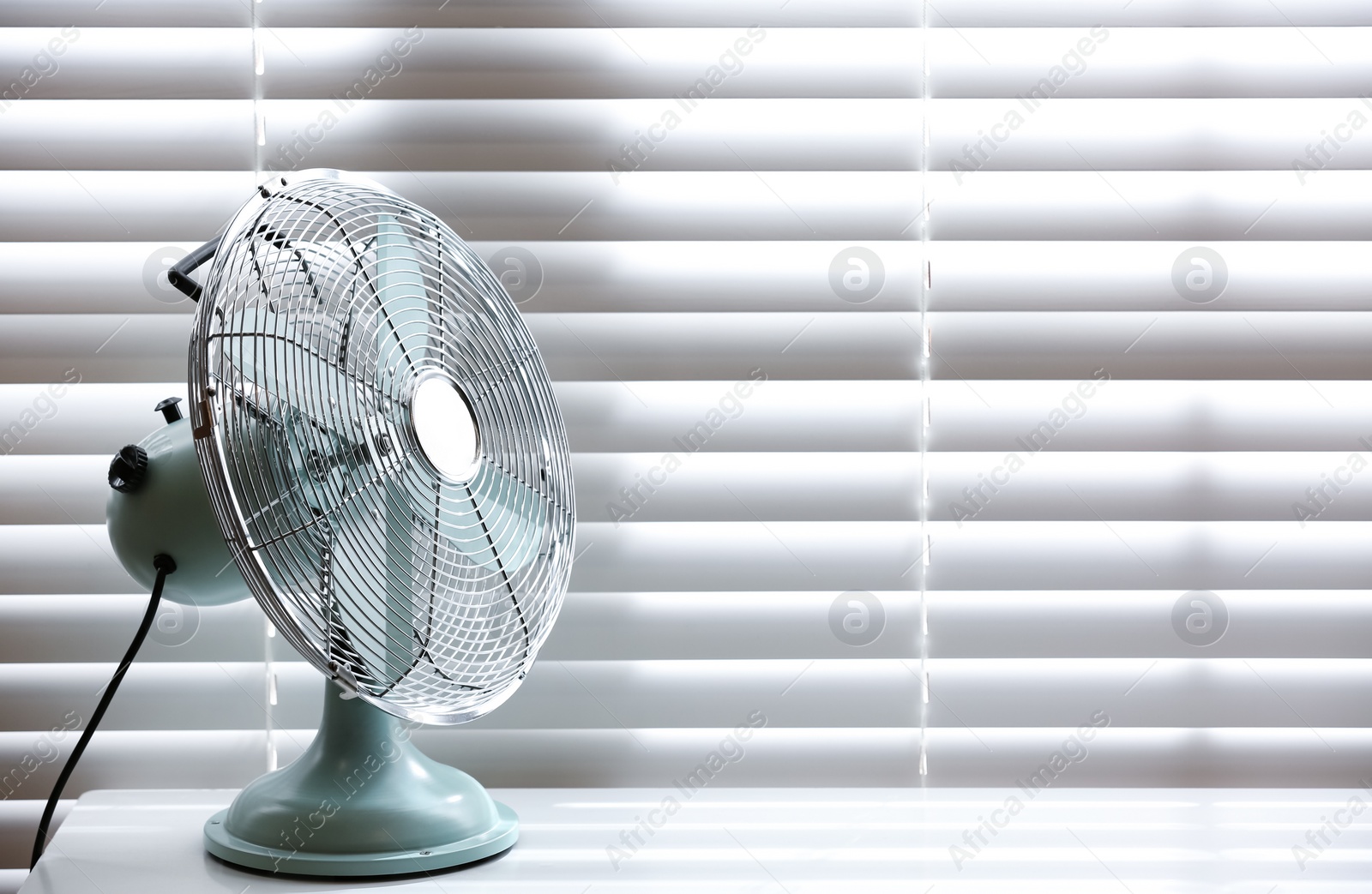 Photo of Modern electric fan on table near window indoors. Space for text