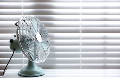 Modern electric fan on table near window indoors. Space for text