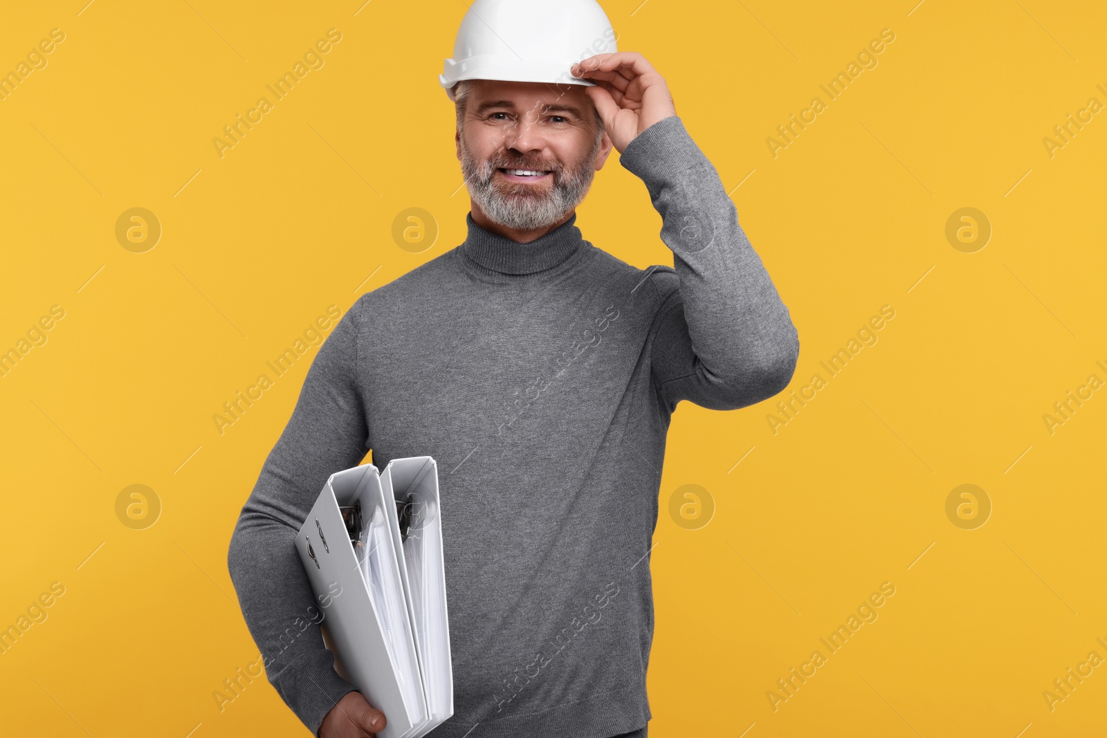 Photo of Architect in hard hat holding folders on orange background