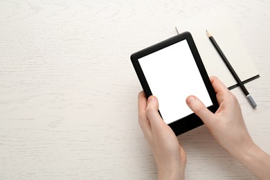 Woman using e-book reader at white wooden table, top view. Space for text