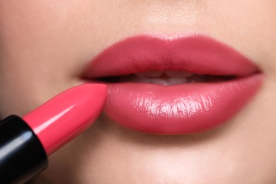 Photo of Closeup view of young woman applying beautiful glossy lipstick