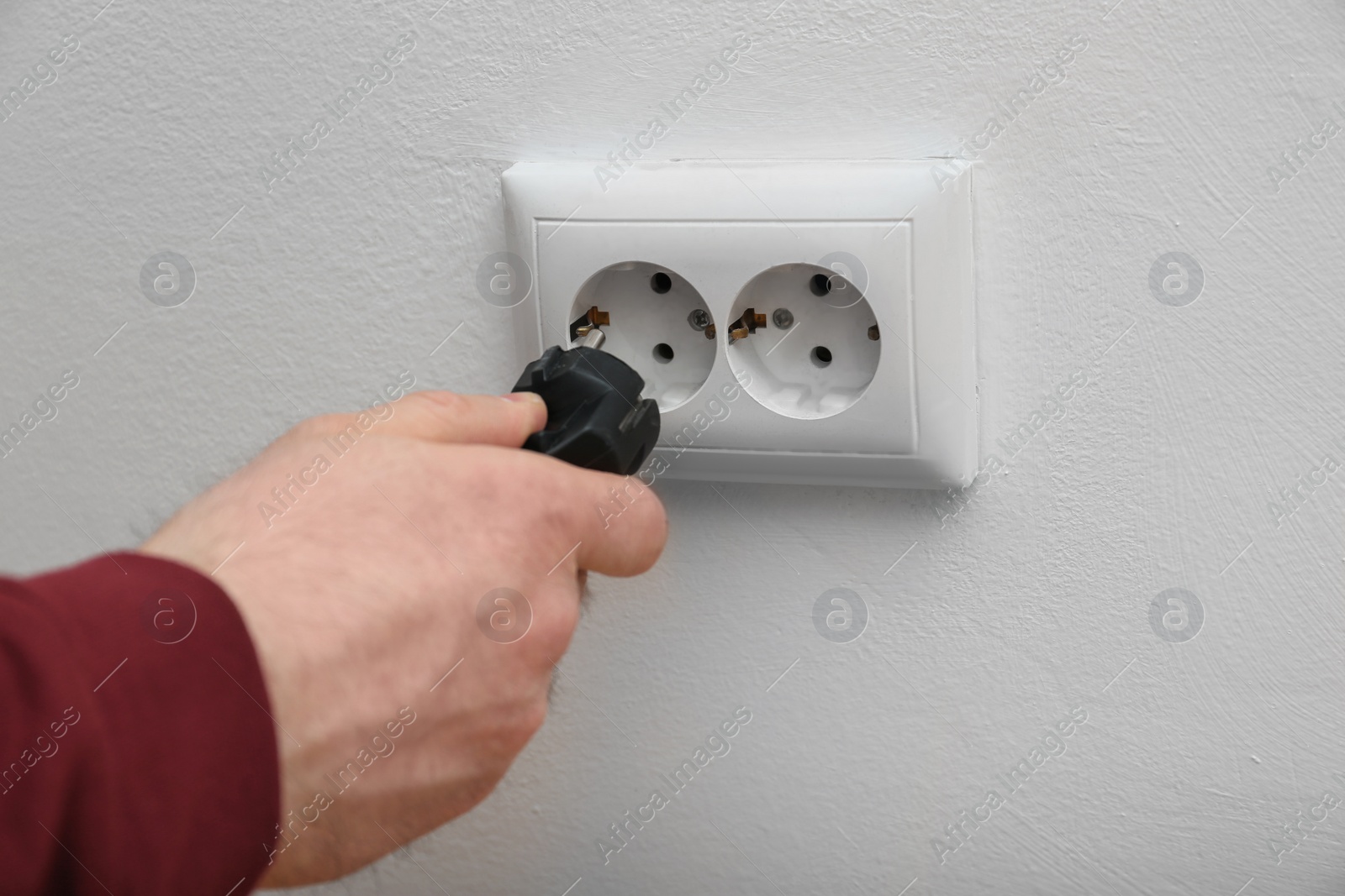 Photo of Electrician inserting plug into power socket on white background, closeup