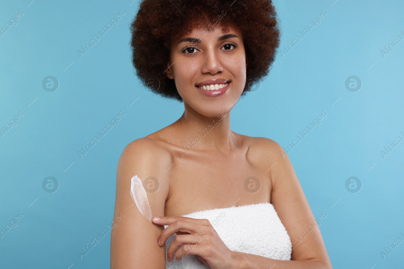 Photo of Beautiful young woman applying body cream onto arm on light blue background