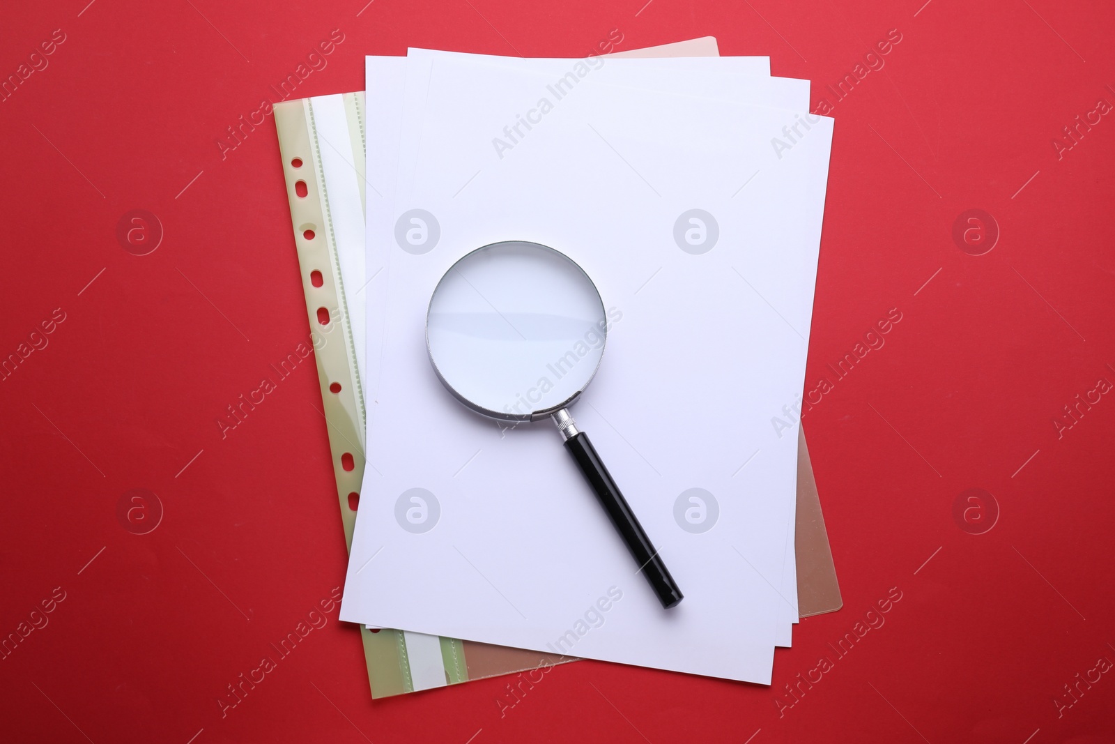 Photo of Magnifying glass and folder with paper sheets on red background, top view