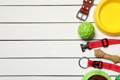Photo of Flat lay composition with dog collars, toys and bowl on white wooden table. Space for text