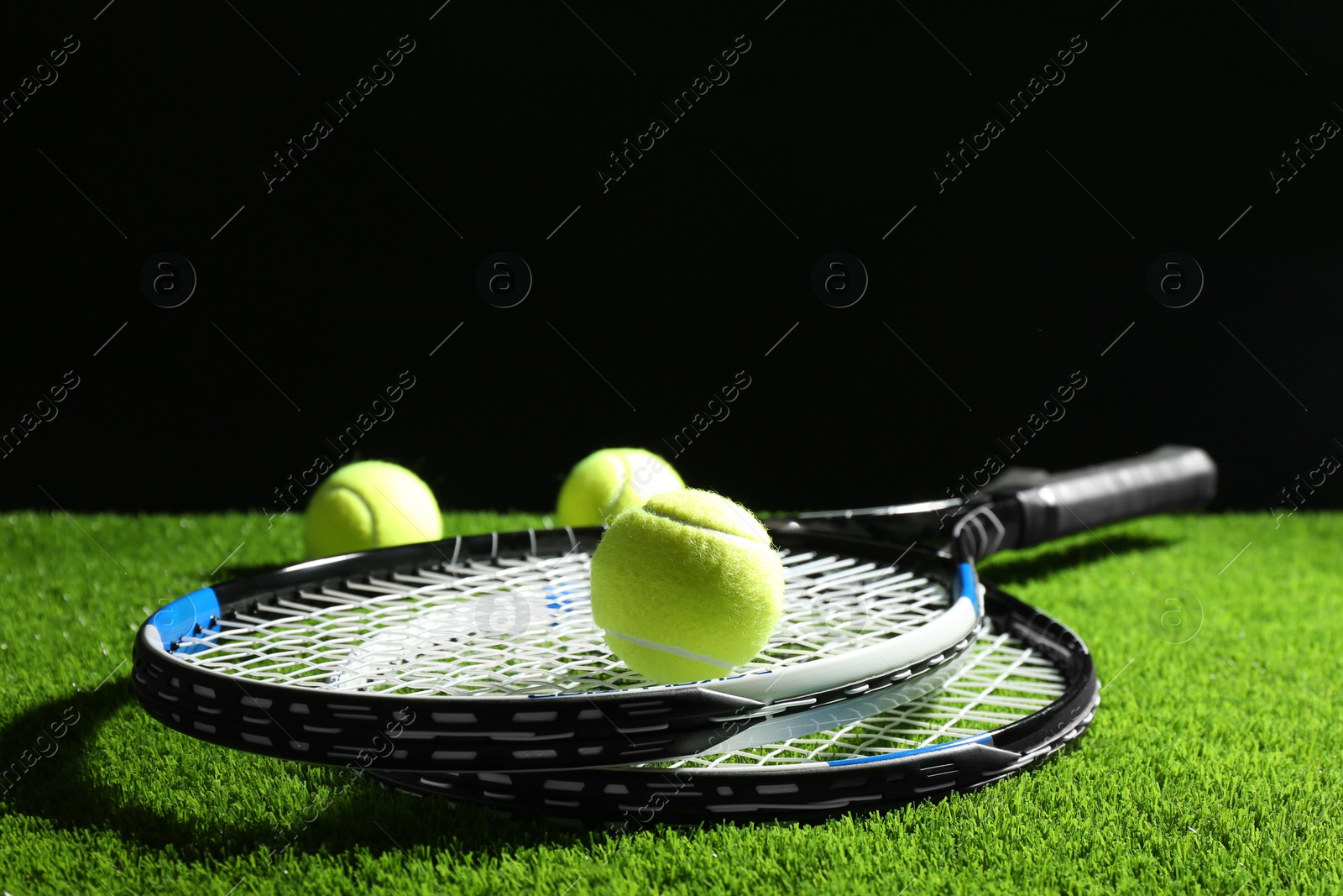 Photo of Tennis rackets and balls on green grass against dark background. Space for text