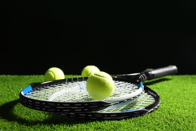 Tennis rackets and balls on green grass against dark background. Space for text