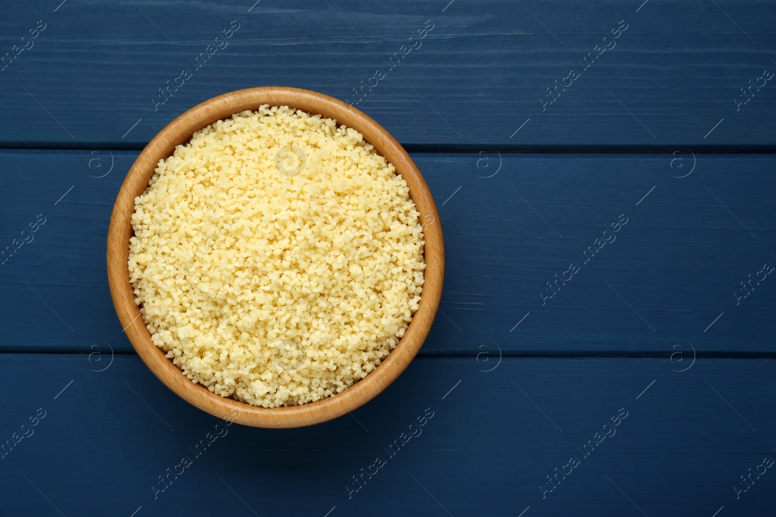 Photo of Bowl of tasty couscous on blue wooden table, top view. Space for text