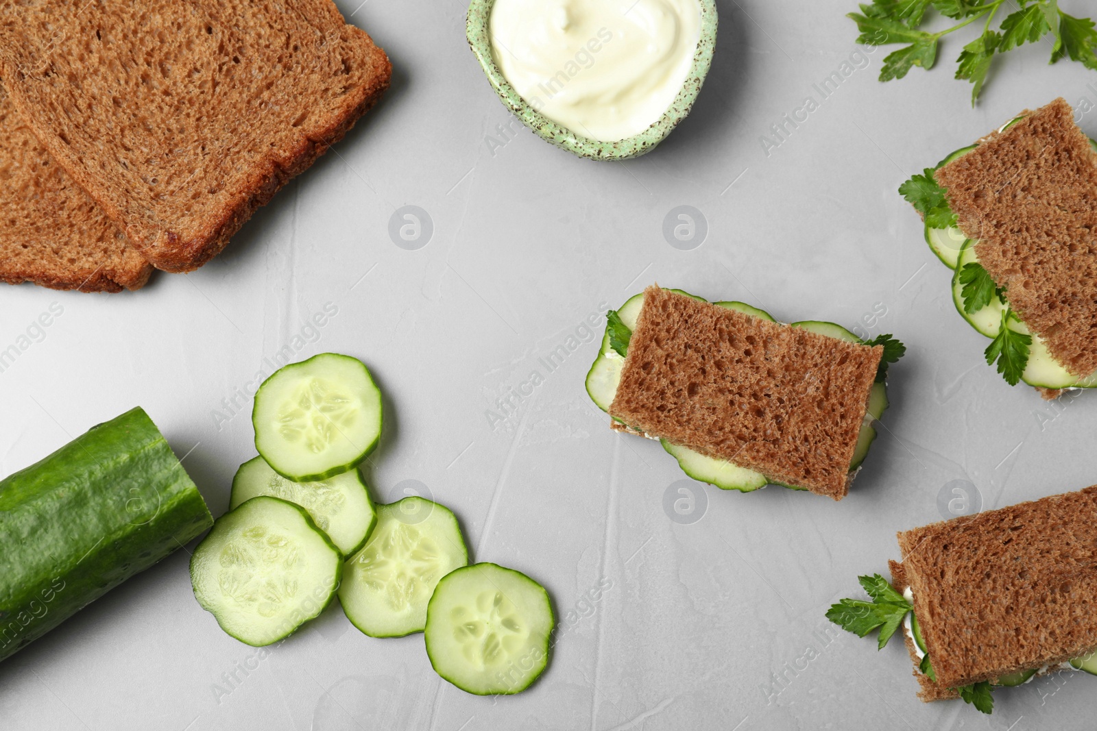 Photo of Flat lay composition with traditional English cucumber sandwiches and ingredients on grey background