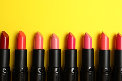 Many bright lipsticks on yellow background, flat lay. Space for text