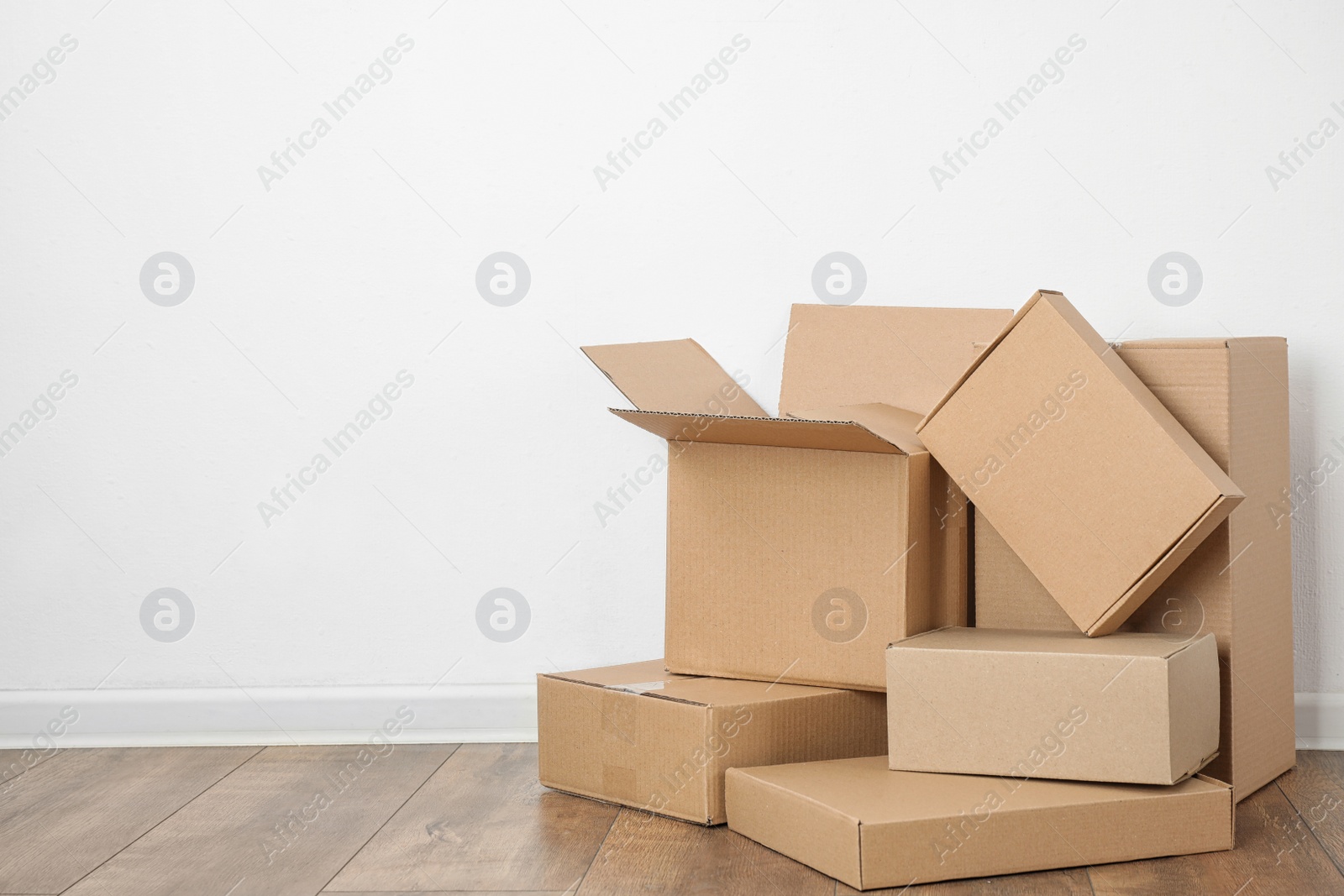 Photo of Pile of cardboard boxes near white wall indoors. Space for text