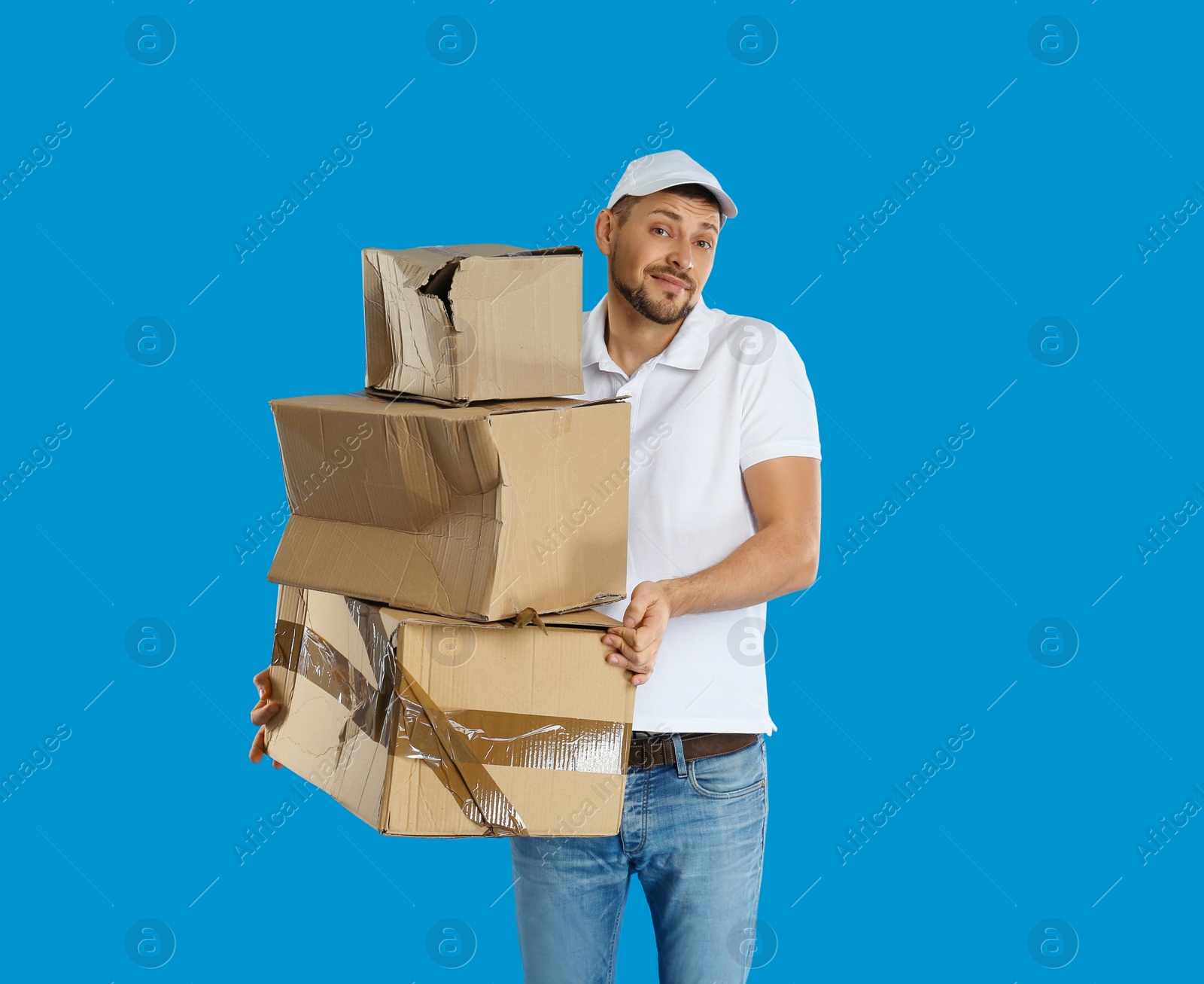 Photo of Emotional courier with damaged cardboard boxes on blue background. Poor quality delivery service