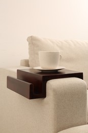 Photo of Cup of coffee on sofa with wooden armrest table indoors. Interior element