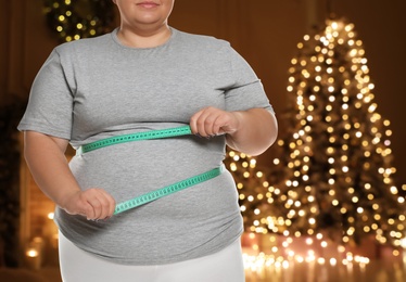 Image of Overweight woman measuring her waist in room with Christmas tree after holidays, closeup