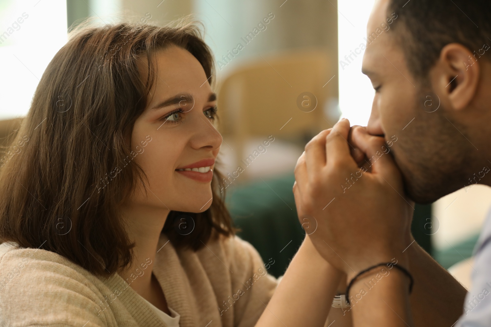 Photo of Romantic date. Guy kissing his girlfriend's hands indoors