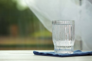 Glass of pure water on white table, space for text
