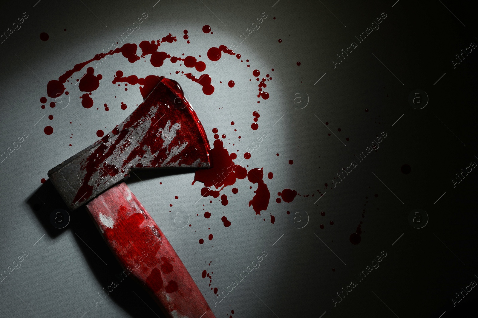 Photo of Axe with blood on gray surface in darkness, top view. Space for text