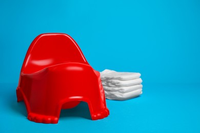 Photo of Red baby potty and stack of diapers isolated on light blue background, space for text. Toilet training