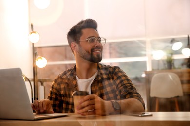 Photo of Man with cup of coffee working on laptop at table in cafe