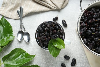 Colander and cup of delicious ripe black mulberries on grey table, flat lay