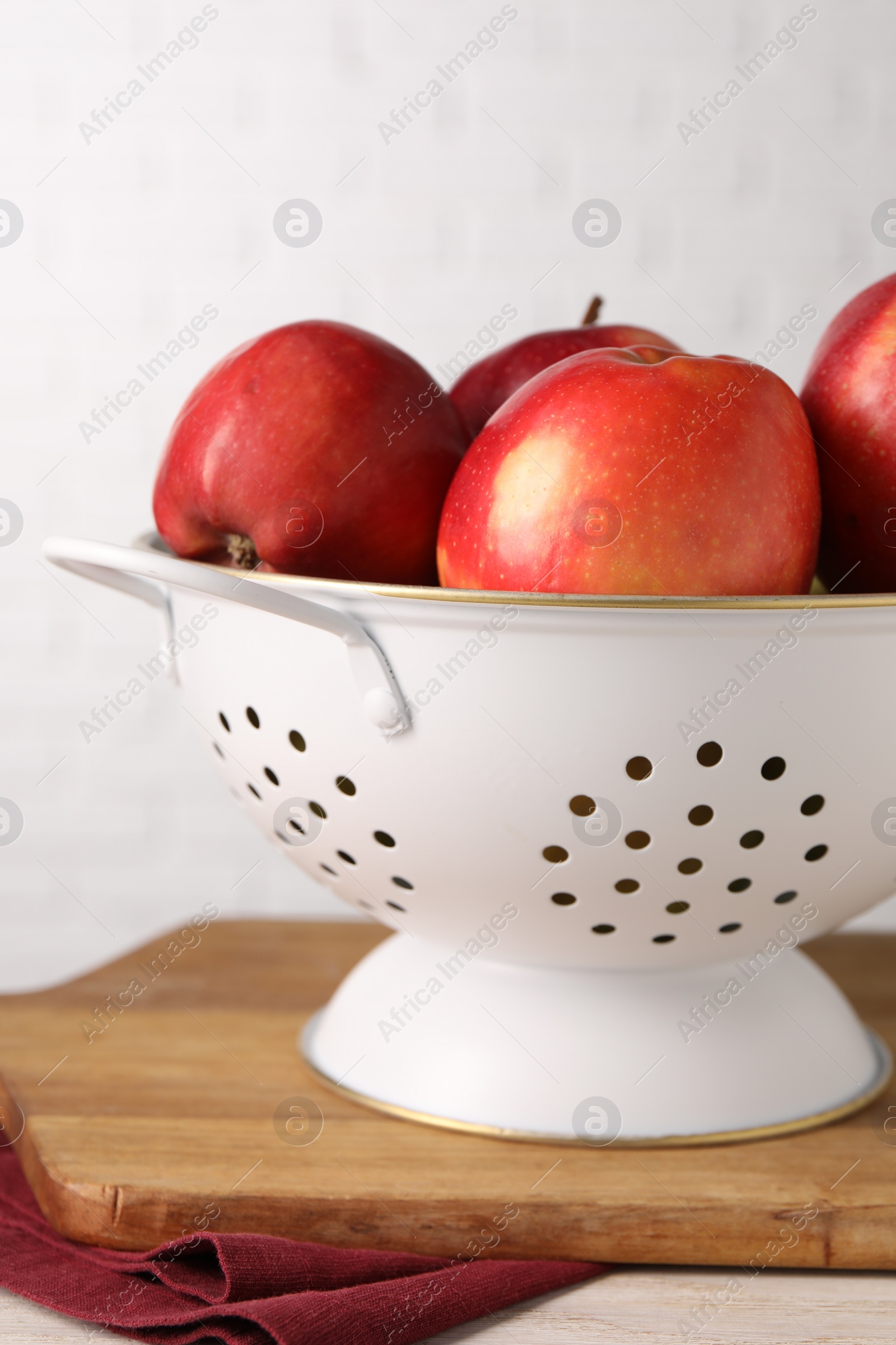 Photo of Fresh apples in colander on white wooden table, closeup