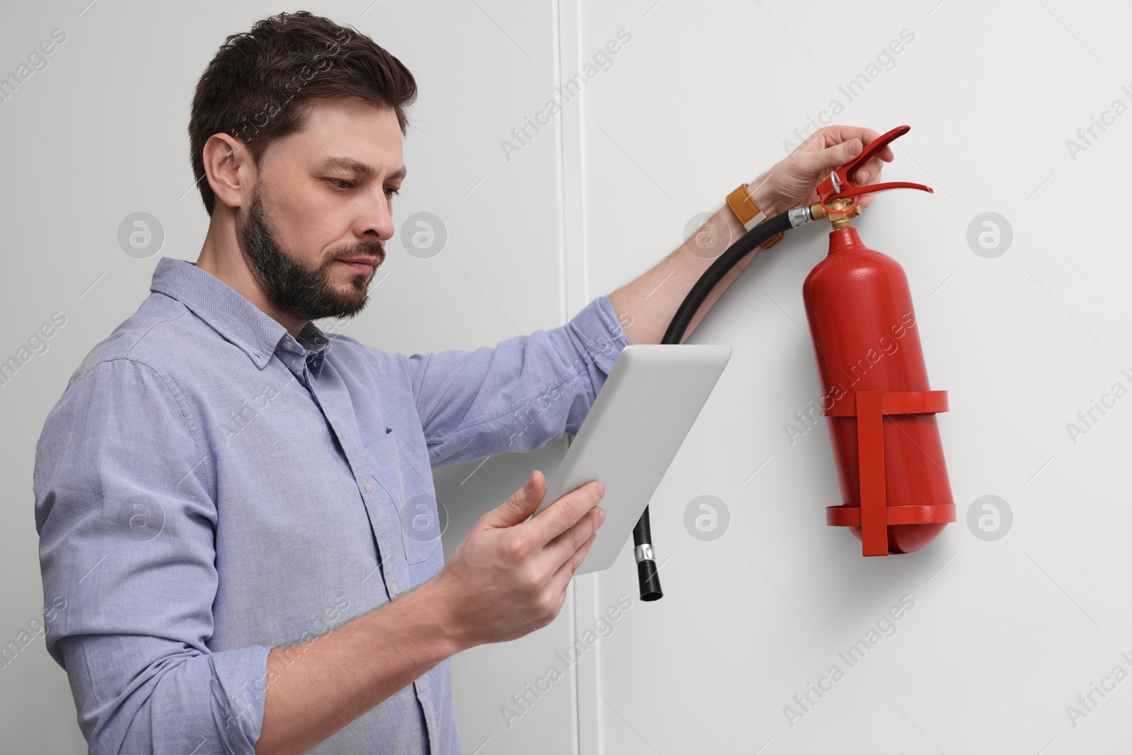 Photo of Man with tablet checking fire extinguisher indoors