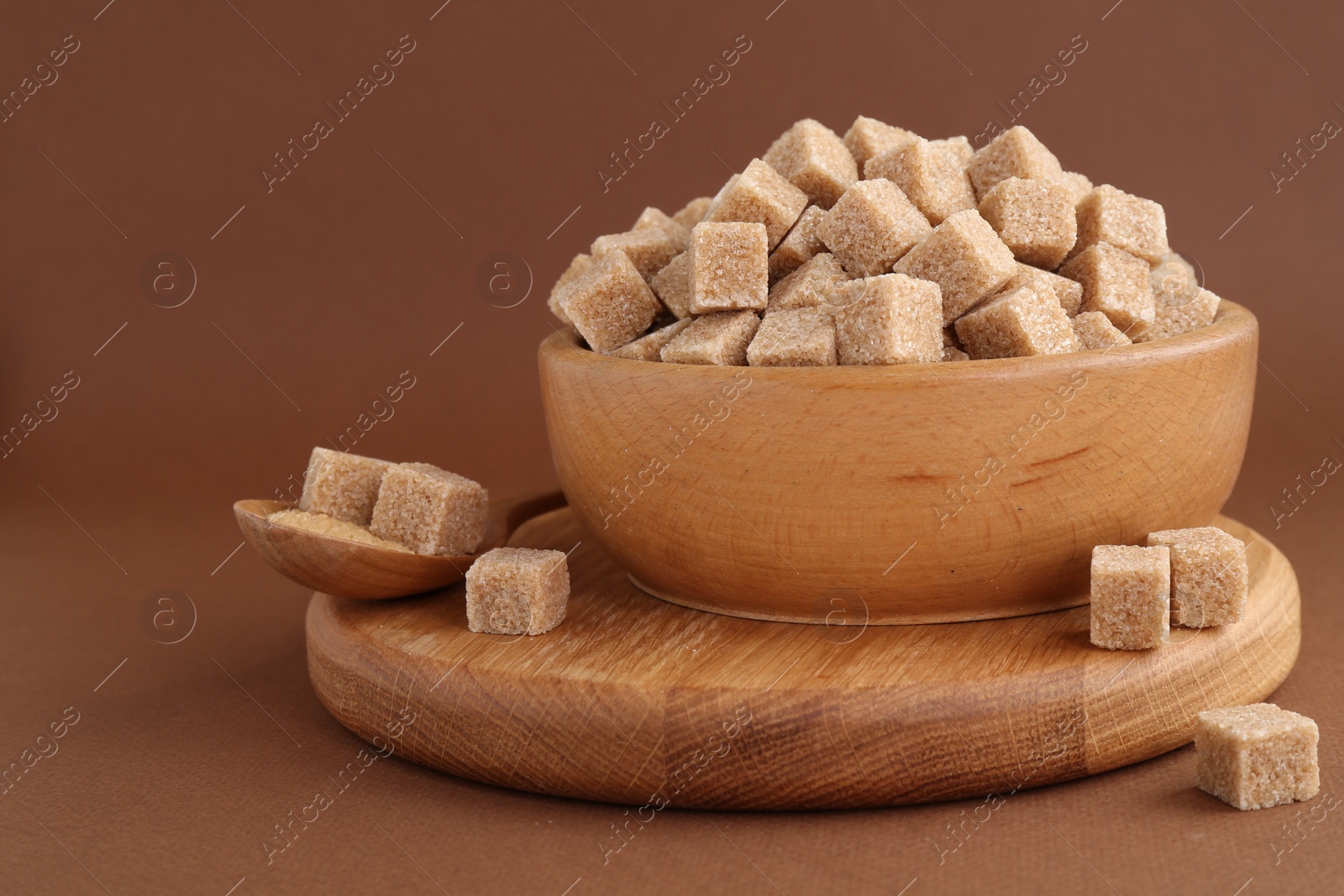 Photo of Brown sugar cubes in bowl and spoon on color background