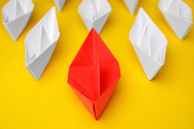 Photo of Group of paper boats following red one on yellow background, closeup. Leadership concept